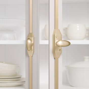 Glass front kitchen cabinet with gold hardware showing white plates and bowls inside behind the doors