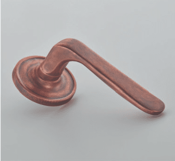 Copper door lever with round backplate detached from a door resting on a gray surface