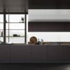 Modern dark kitchen with island, open metal shelving, and a large window wall showing outdoors.