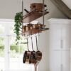 Copper pots and pans hanging from a ceiling pot rack in a bright kitchen, with green trailing plant and white cabinets nearby.