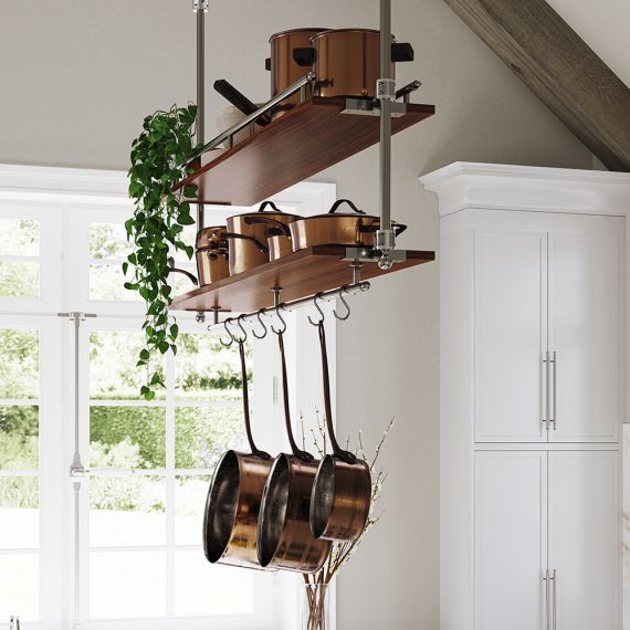 Copper pots and pans hanging from a ceiling pot rack in a bright kitchen, with green trailing plant and white cabinets nearby.